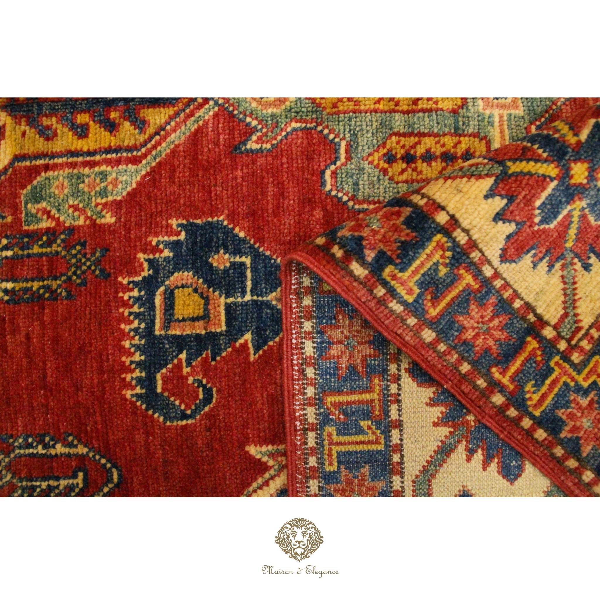 Close-up of a red and patterned rug with a brand logo at the bottom.