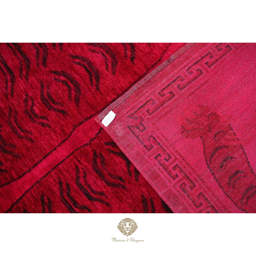 Close-up of a red fabric with intricate patterns, featuring a brand logo at the bottom.