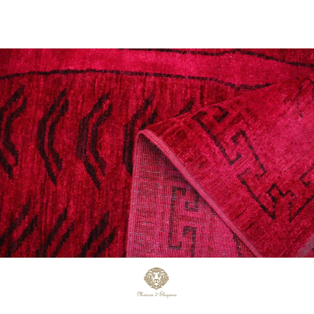 Close-up of a red textured fabric with black patterns, featuring a brand logo at the bottom.