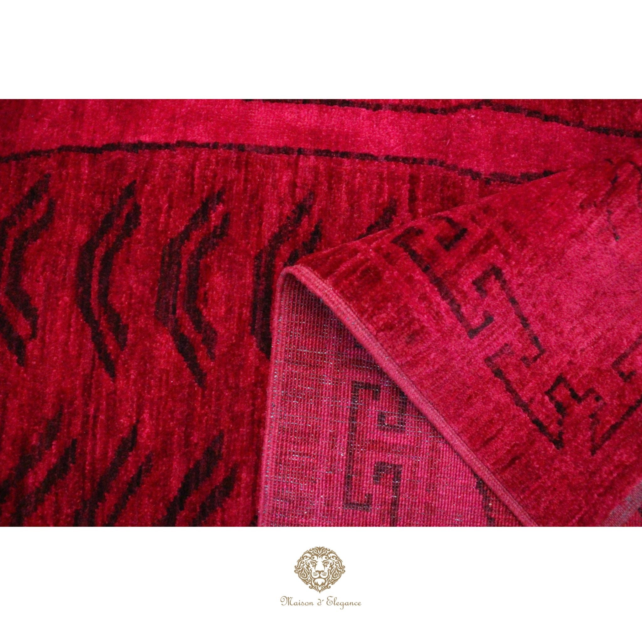 Close-up of a red textured fabric with black patterns, featuring a brand logo at the bottom.