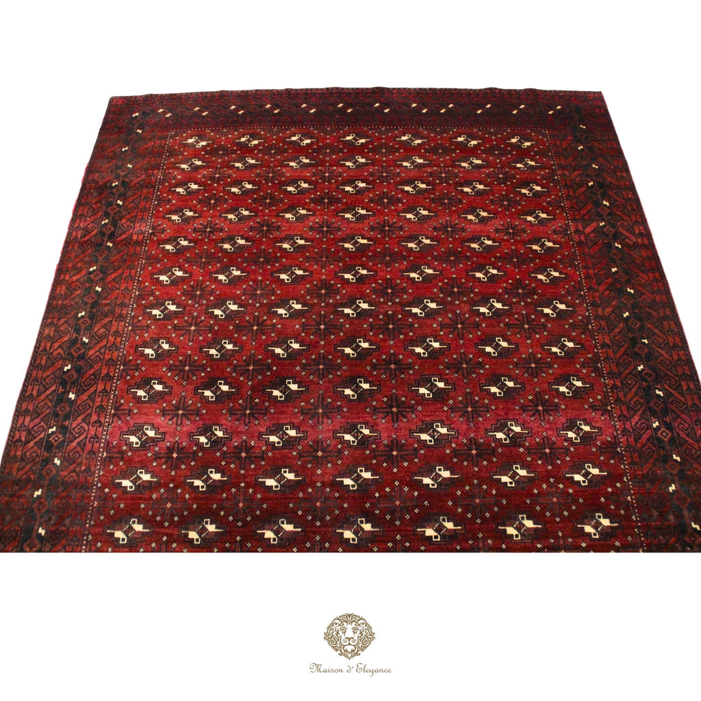 Red patterned rug with a brand logo at the bottom right corner on a red background