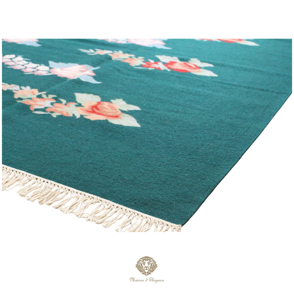 Teal throw blanket with floral patterns and fringes on a green background