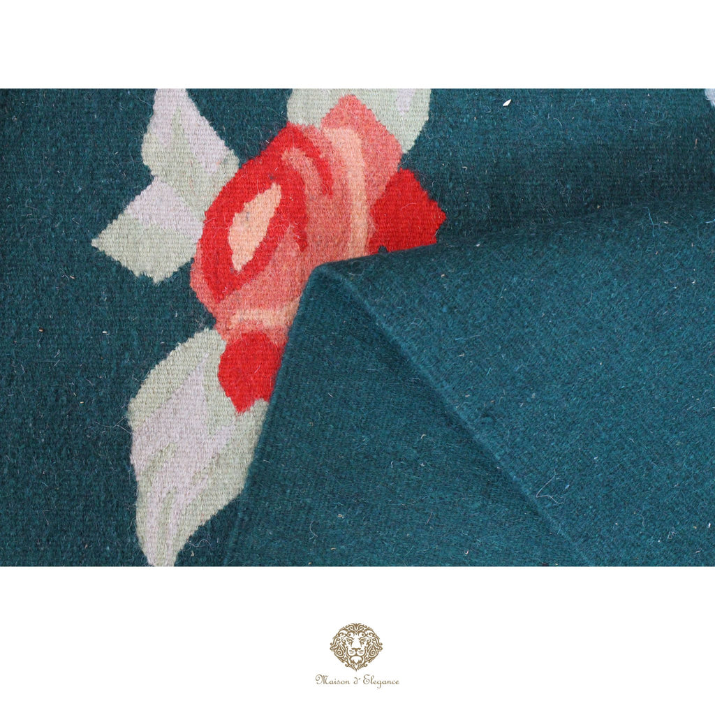 Close-up of teal fabric with a floral pattern, featuring a red flower and green leaves.