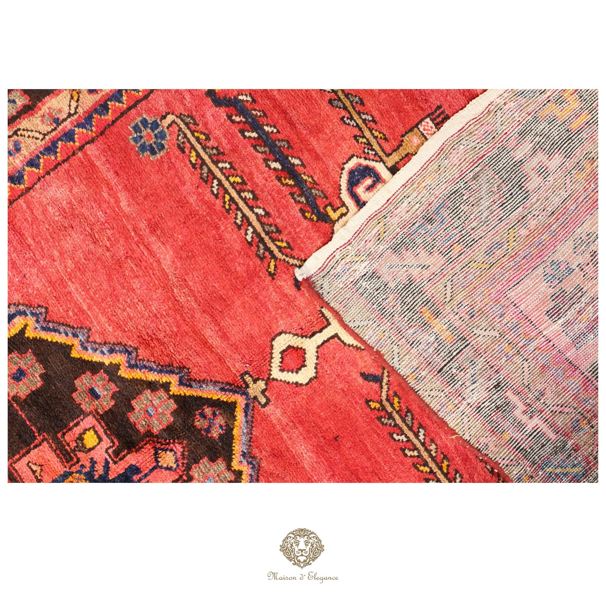 Close-up of a red patterned rug with a brand logo in the corner.