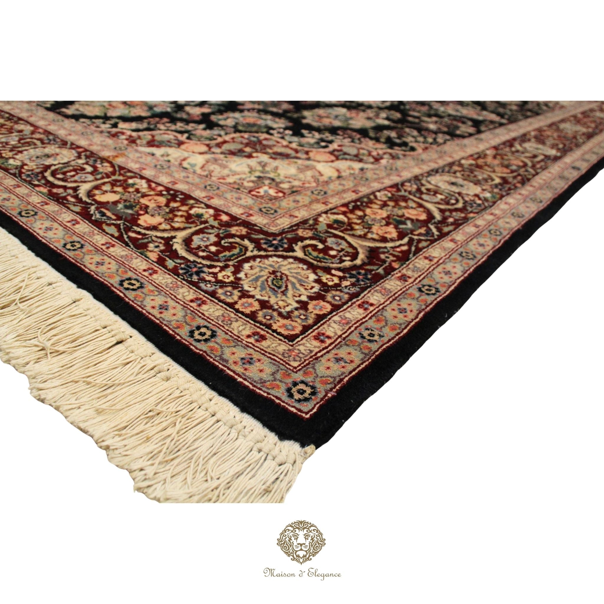 Corner of a patterned rug with tassels on a Brown background, featuring a brand logo.