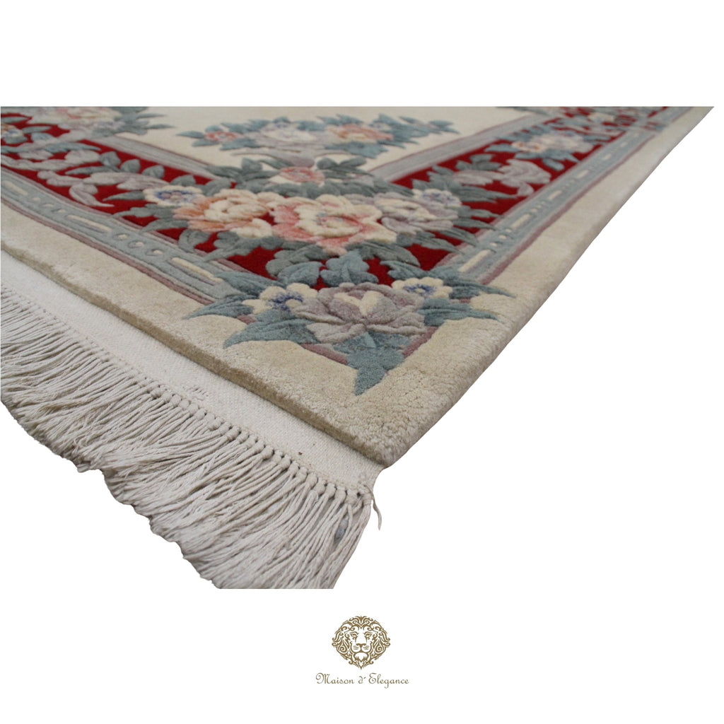 Corner of a decorative rug with floral patterns and fringes on a white background