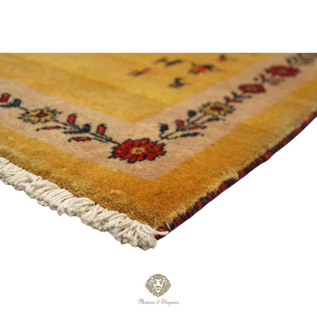 Corner of a yellow rug with floral patterns and white fringe on a  gold background