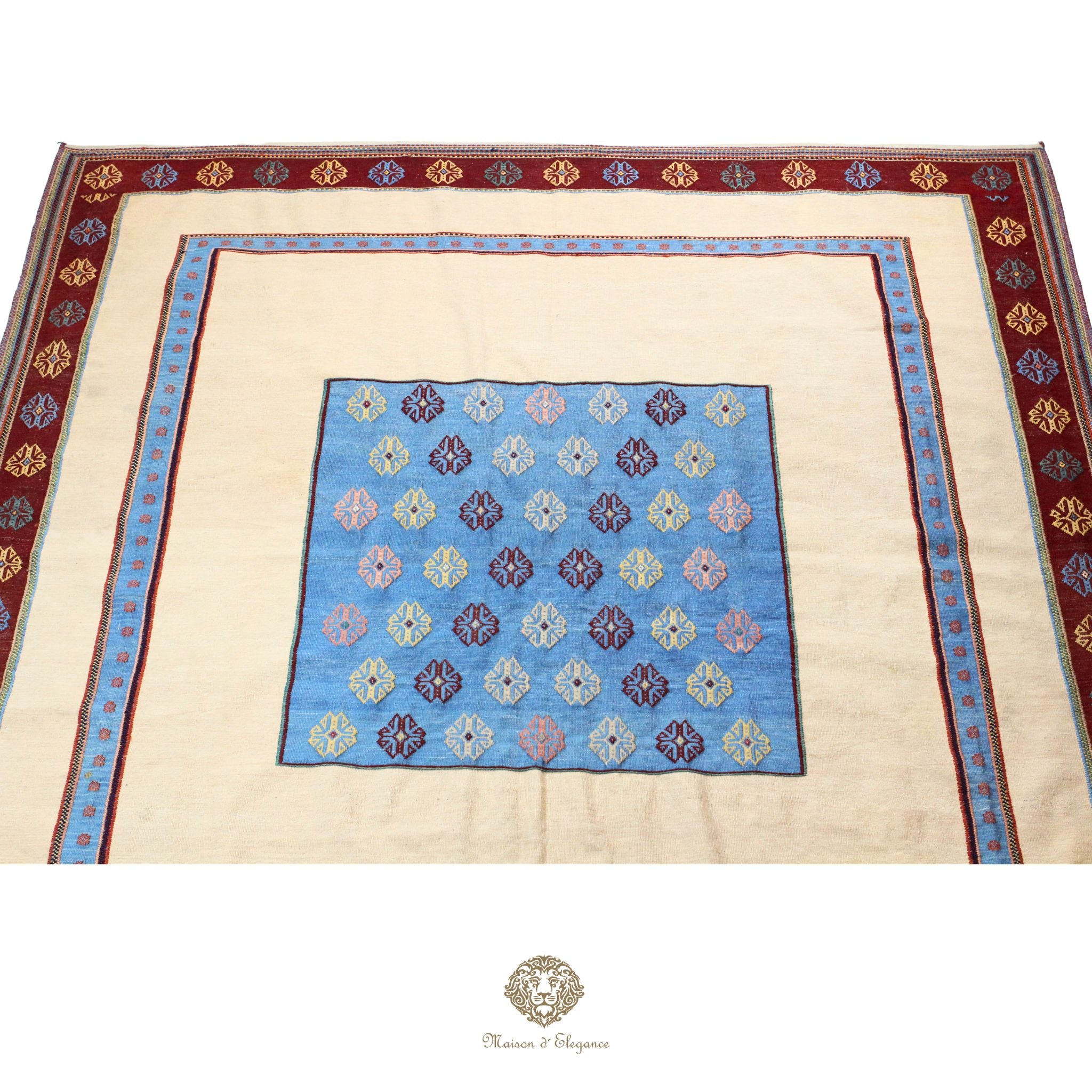 Decorative rug with a blue floral pattern and beige border, featuring a brand logo at the bottom.