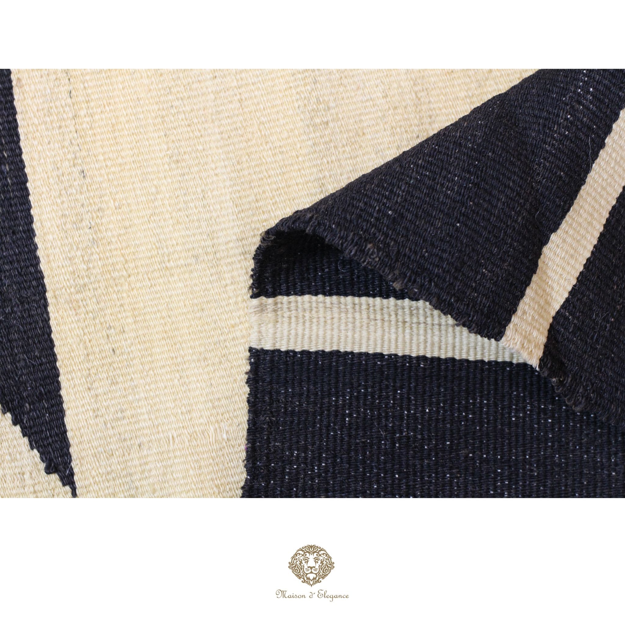 Close-up of a textured fabric with black and beige pattern, featuring a brand logo at the bottom.