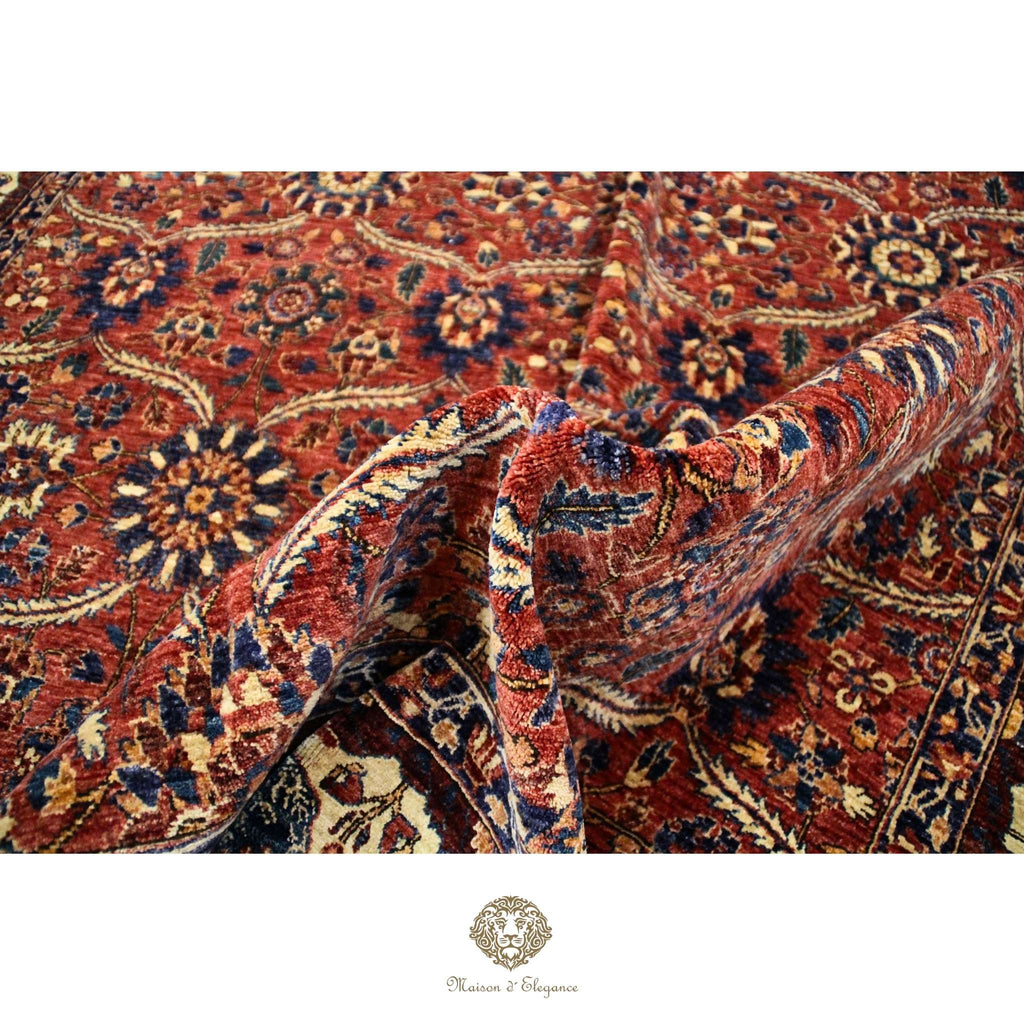 Close-up of a patterned fabric with intricate designs on a red background, featuring a brand logo.