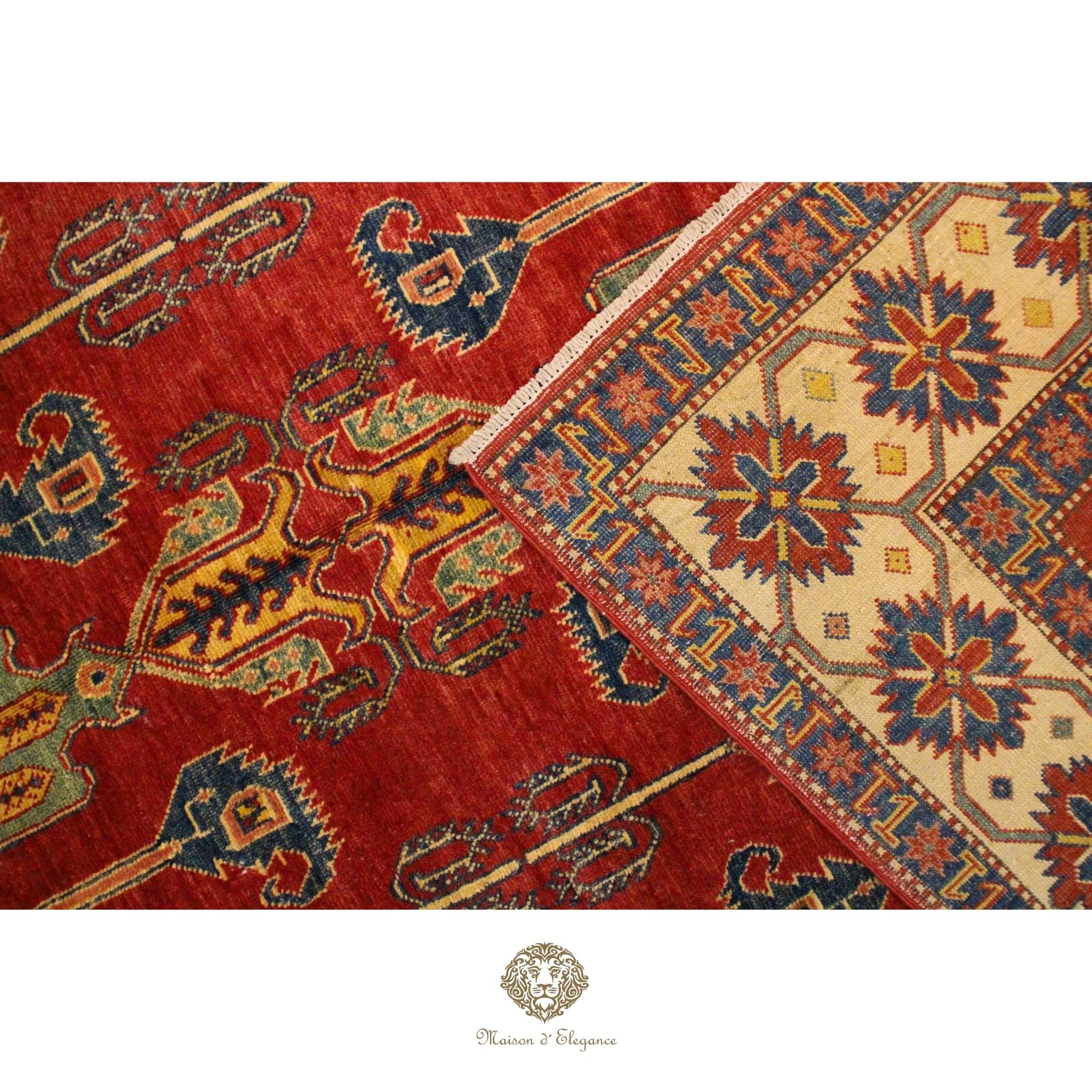Close-up of a red and patterned rug with a brand logo at the bottom.