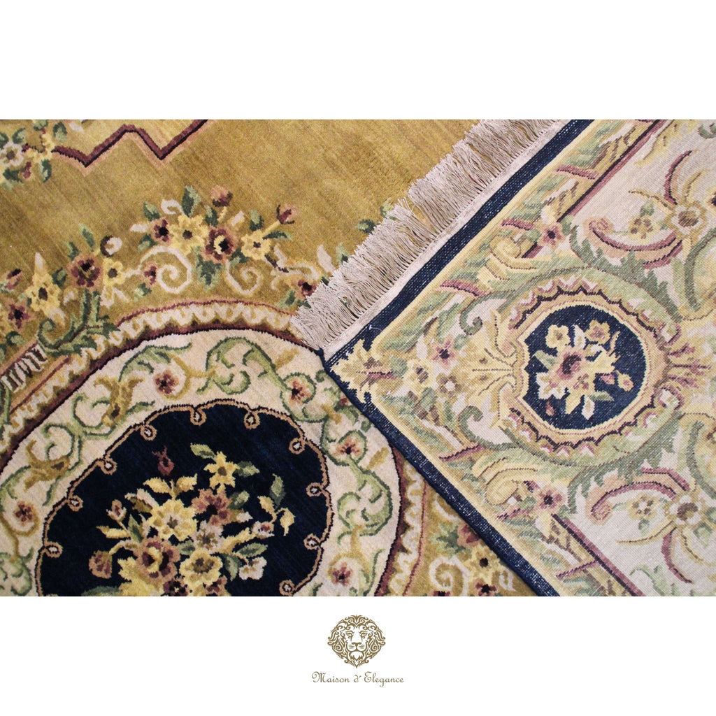 Close-up of an intricately designed rug with floral patterns and a brand logo at the bottom.