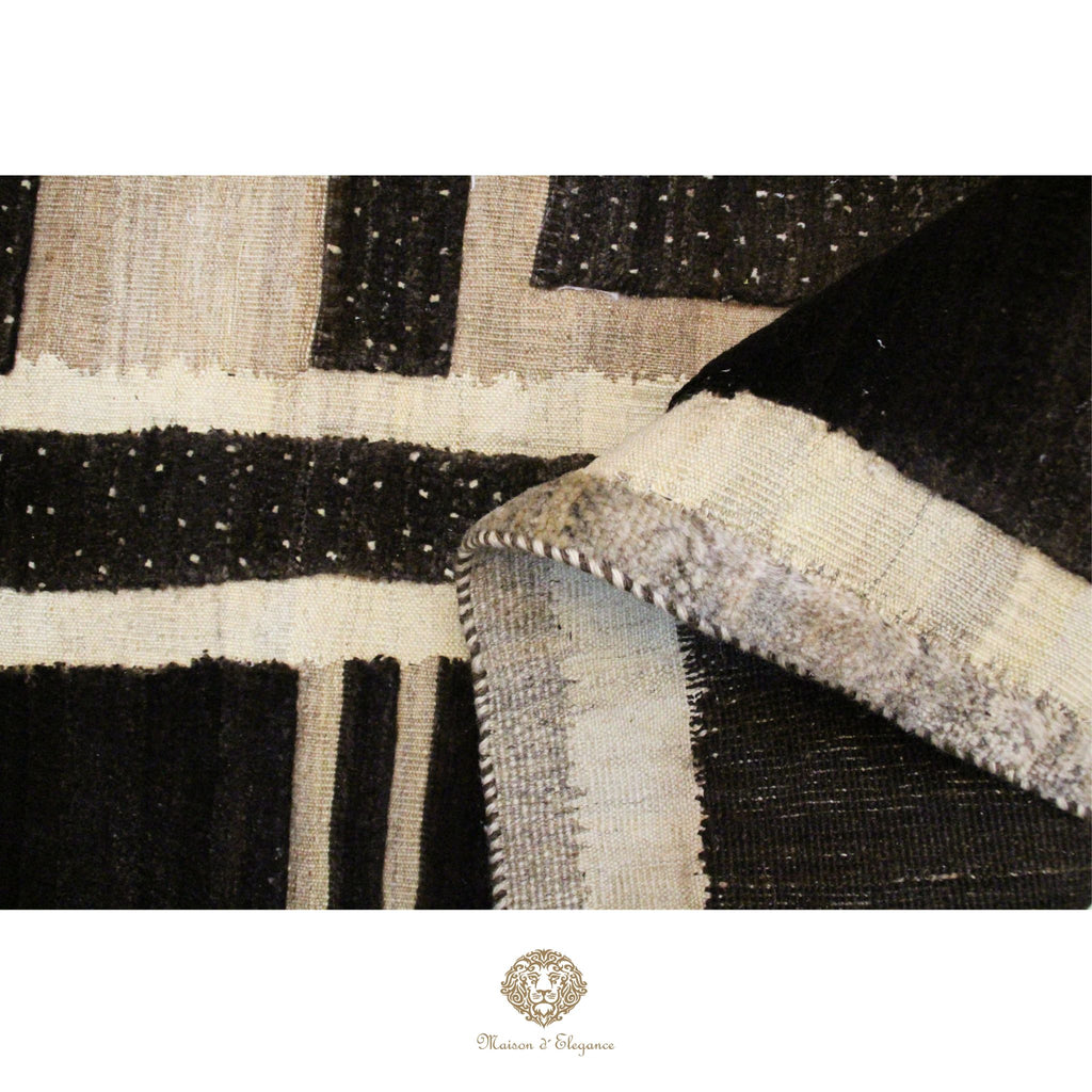 Close-up of a textured black, white, and beige rug with a brand logo at the bottom.