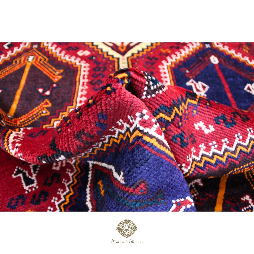 Close-up of intricately patterned fabric with vibrant colors and a brand logo at the bottom.