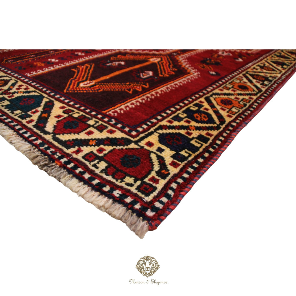 Corner of a patterned rug with intricate designs on a red background